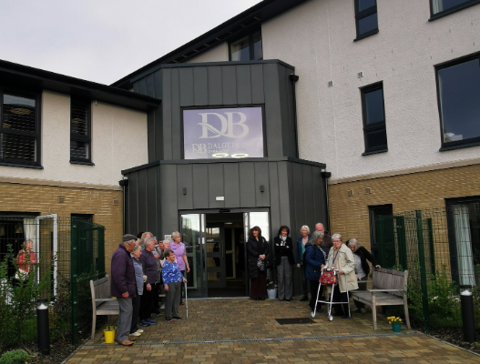 Residents, staff, and guests gathered at Dalgety Bay Care Home’s first birthday celebration, featuring colourful decorations, a ribbon-cutting ceremony, and live bagpipe music.