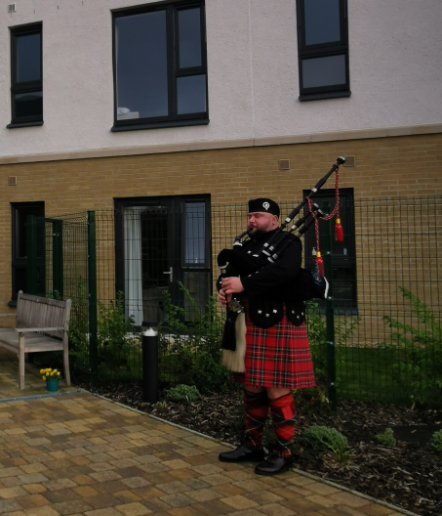 Residents, staff, and guests gathered at Dalgety Bay Care Home’s first birthday celebration, featuring colourful decorations, a ribbon-cutting ceremony, and live bagpipe music.