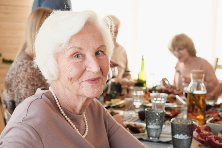 older woman smiling while she enjoys dinner at the care home with her family