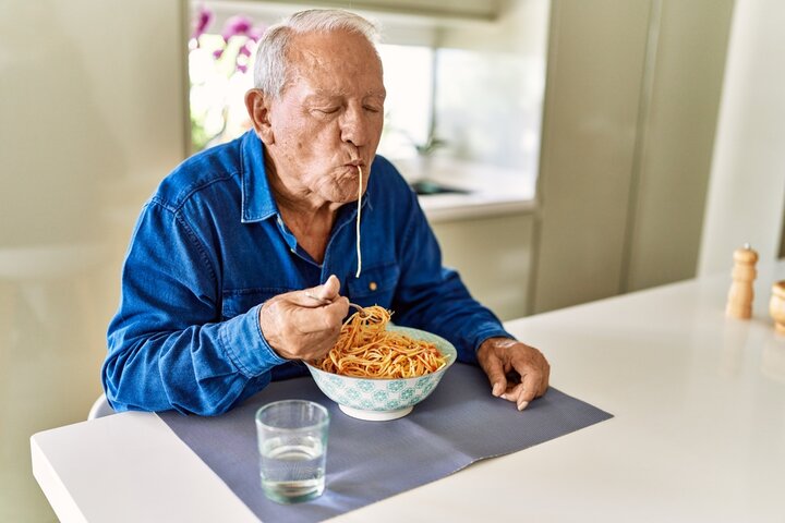 Senior man eating spaghetti at kitchen