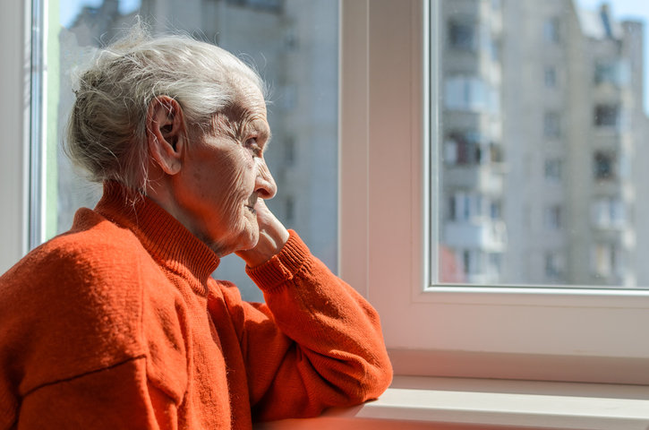 older woman looking out her window at home