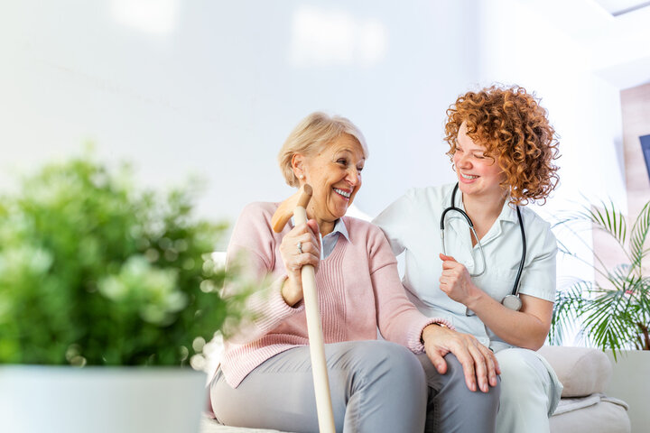 resident and care giver on a sofa smiling at each other in care home